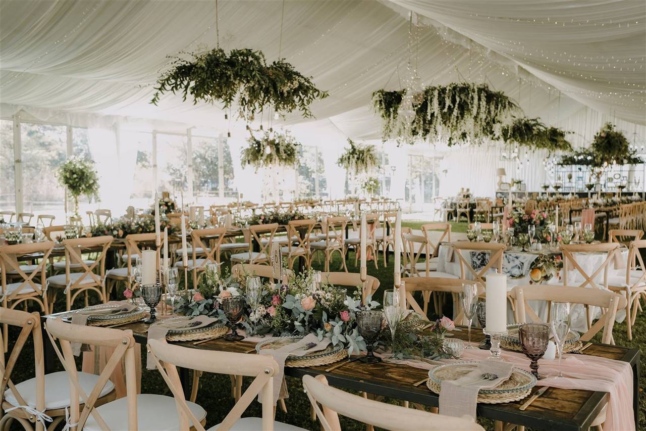 Montaje del salón: mesas con vajilla, velas y arreglos florales bajo carpa con guirnaldas de luces